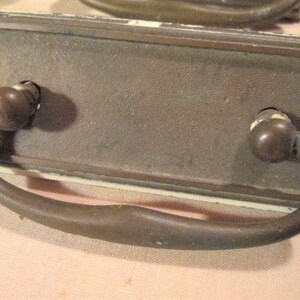 May include: A vintage brass drawer pull with a curved handle and two round knobs. The pull is mounted on a rectangular plate with a white background.