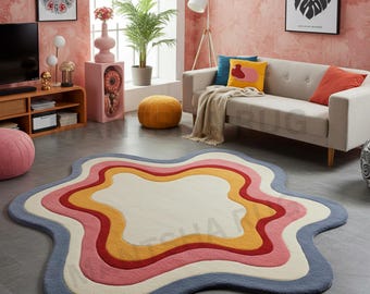 May include: An irregular, star-shaped area rug featuring concentric, wavy layers of color including cream, yellow, red, pink, and blue. The rug has a thick, tufted texture and is positioned on a flat, gray floor in a living room setting.