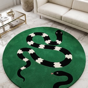 May include: A round green rug featuring a large, winding snake with a black and white striped pattern across its body, and a smaller solid black snake with a pink tongue positioned near the bottom edge of the circular floor covering.