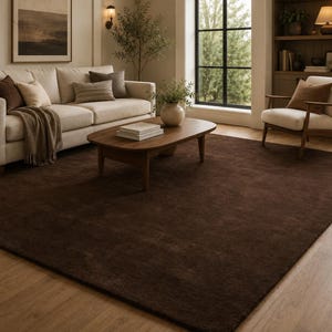May include: A large, rectangular area rug in a solid, deep chocolate brown color with a soft, plush texture. The rug is positioned on a light-toned wooden floor, covering a significant portion of the space beneath a wooden coffee table and sofa.