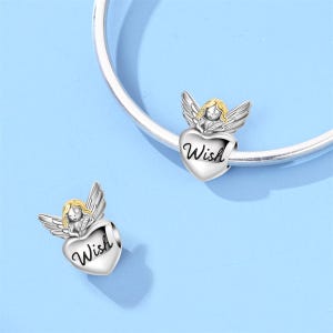 May include: Two silver-toned angel charms with gold hair and wings, each holding a heart-shaped charm with the word "Wish" in cursive. The charms are displayed on a silver bracelet against a light blue background.