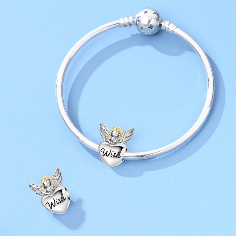 May include: A silver bracelet with a star-shaped clasp and two charms. Each charm features a small angel with gold hair and wings, holding a heart-shaped pendant with the word "Wish" engraved on it. The background is a light blue.