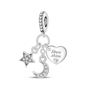May include: A silver charm featuring a dangling star, crescent moon, and heart. The star and moon are encrusted with clear stones. The heart is engraved with the text Stars shine and includes a small clear stone at the bottom.