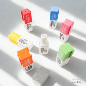 May include: A selection of aromatherapy inhalers with coloured caps in red, blue, pink, green, yellow, and orange. Each inhaler is labelled with the text "DUMBLE INHALER V2". A white aromatherapy bottle and a grey soap are also present.