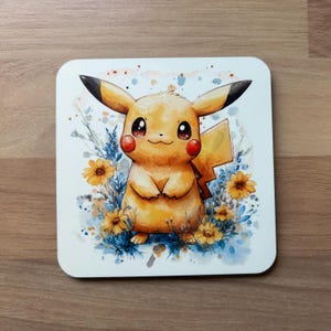 May include: A square coaster featuring a watercolor illustration of Pikachu, the popular Pokémon character. The yellow Pikachu is surrounded by yellow flowers and blue foliage. The coaster has a white background.