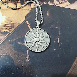 Può includere: Un ciondolo circolare color argento caratterizzato da un design a sole in rilievo con raggi ondulati che si irradiano da una sfera centrale. Il ciondolo è sospeso a una catenina a maglia quadrata abbinata con finitura metallica liscia e lucida.