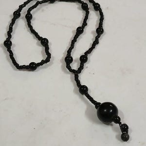 以下が含まれることがあります： 黒いビーズのロザリオネックレス。大きな中央のビーズと小さなビーズが付いています。ネックレスは黒いビーズを黒い糸で繋いで作られています。ビーズは丸く滑らかです。