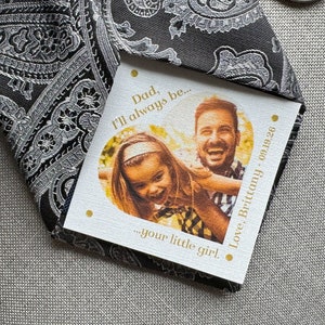 May include: A white card with gold lettering and a photo of a father and daughter. The card reads "Dad, I'll always be... your little girl. Love, Brittany 09.19.26"