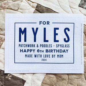May include: A white card with navy blue text that reads "FOR MYLES" at the top. Below, it says "PATCHWORK & POODLES - SPYGLASS" and "HAPPY 6TH BIRTHDAY." The card is labeled "MADE WITH LOVE BY MOM 2024."