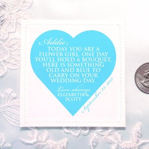 May include: A white card with a blue heart shape and the text "Addie, TODAY YOU ARE A FLOWER GIRL, ONE DAY YOU'LL HOLD A BOUQUET, HERE IS SOMETHING OLD AND BLUE TO CARRY ON YOUR WEDDING DAY. Love always, ELIZABETH & SCOTT September 23, 2017".
