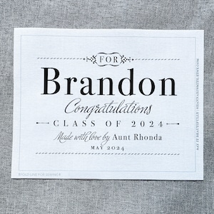 May include: A white tag with black text that reads "FOR Brandon Congratulations CLASS OF 2024 Made with love by Aunt Rhonda MAY 2024".