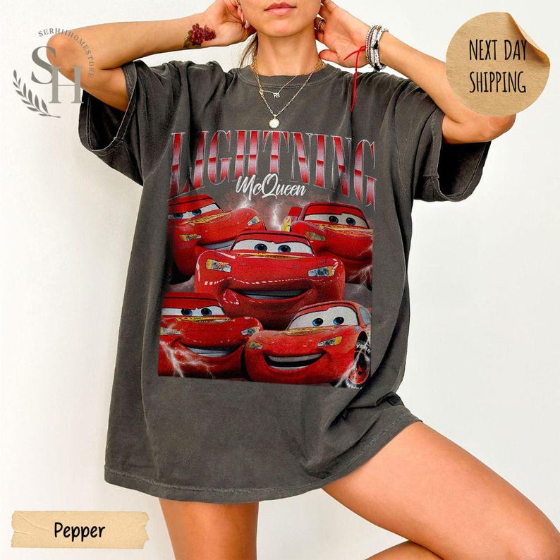 Puede incluir: Camiseta gris oscuro con un dise&ntilde;o de Rayo McQueen de la pel&iacute;cula Cars. El texto "LIGHTNING McQueen" est&aacute; impreso sobre la imagen del coche de carreras rojo. La camiseta tiene un corte holgado.