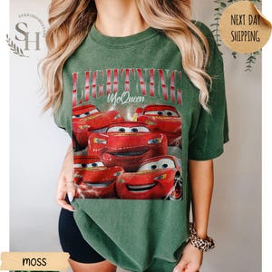 Puede incluir: Camiseta verde musgo con un gr&aacute;fico de Rayo McQueen de la pel&iacute;cula Cars. El dise&ntilde;o incluye el texto "LIGHTNING McQueen" en rojo y blanco. El gr&aacute;fico muestra m&uacute;ltiples im&aacute;genes del coche de carreras rojo.