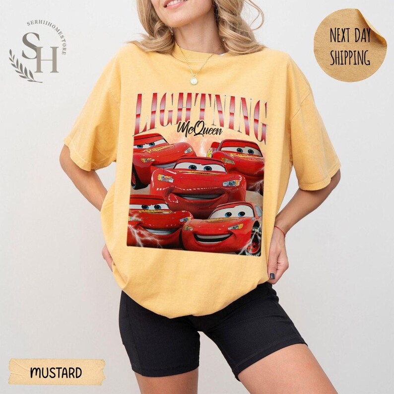 Puede incluir: Camiseta de color mostaza con un dise&ntilde;o de Rayo McQueen de la pel&iacute;cula Cars. El dise&ntilde;o incluye el texto "LIGHTNING McQueen" en rojo y blanco. La camiseta es de corte holgado.