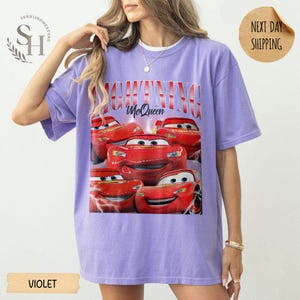 Puede incluir: Camiseta violeta con un dise&ntilde;o de Rayo McQueen de la pel&iacute;cula Cars. El dise&ntilde;o incluye el texto "LIGHTNING McQueen" en rojo y blanco. La camiseta tiene cuello redondo y mangas cortas.