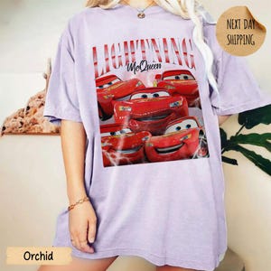Puede incluir: Camiseta color orqu&iacute;dea con un gr&aacute;fico de Rayo McQueen de la pel&iacute;cula Cars. El dise&ntilde;o incluye el texto "LIGHTNING McQueen" en una fuente estilizada, con m&uacute;ltiples im&aacute;genes del coche de carreras rojo. La camiseta tiene un corte holgado.
