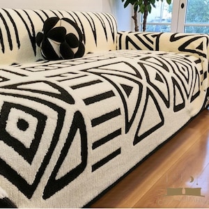 Puede incluir: Un sofá con un patrón geométrico en blanco y negro. El sofá tiene una manta a juego y un cojín decorativo en forma de bola en blanco y negro. El sofá está sobre un piso de madera noble.