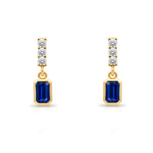 Pode incluir: Um par de brincos pendurados dourados. Cada brinco apresenta uma fileira vertical de três pequenas pedras transparentes acima de uma pedra preciosa retangular azul escuro. Em um fundo branco.