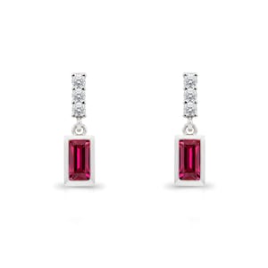 May include: A pair of silver earrings with a vertical rectangular ruby-red gemstone pendant. The top of each earring features a row of small, clear gemstones. The earrings are set against a white background.