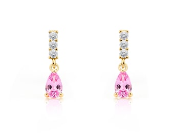 May include: A pair of gold drop earrings. Each earring has a vertical bar with four small, clear stones, connected to a teardrop-shaped pink stone. The earrings are set against a white background.