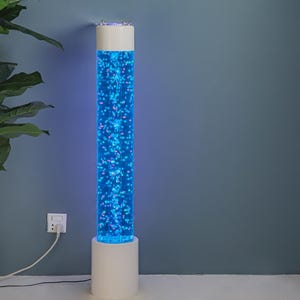 May include: A white and blue bubble tube lamp. The lamp has a cylindrical shape with a white base and top. The tube is filled with blue liquid and bubbles, creating a visually appealing effect. The lamp is plugged into a wall outlet.
