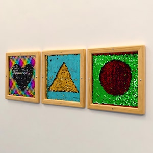May include: Three framed sequin art pieces. The first features a black heart on a rainbow background. The second has a gold triangle on a teal background. The third displays a red circle on a green background. All are in wooden frames.