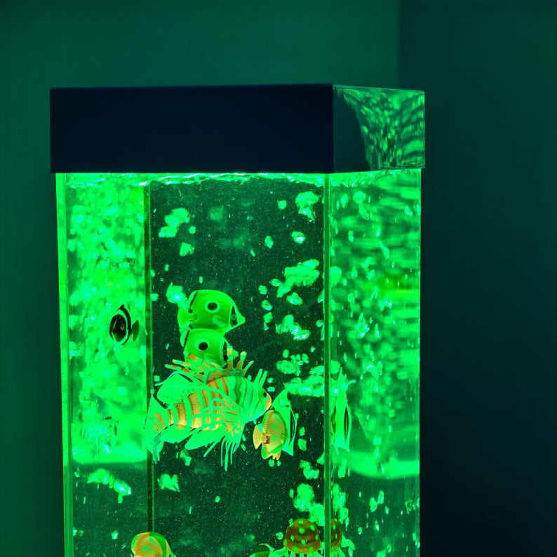 May include: A tall, rectangular aquarium with a black top, illuminated by a vibrant green light. The tank is filled with water and features several colorful, artificial fish. Bubbles rise throughout the tank, creating a dynamic underwater scene.