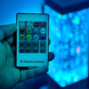 May include: A rectangular RF remote controller with multiple color and function buttons, including green, blue, white, orange, yellow, and cyan. The text "RF Remote Controller" is printed at the bottom.
