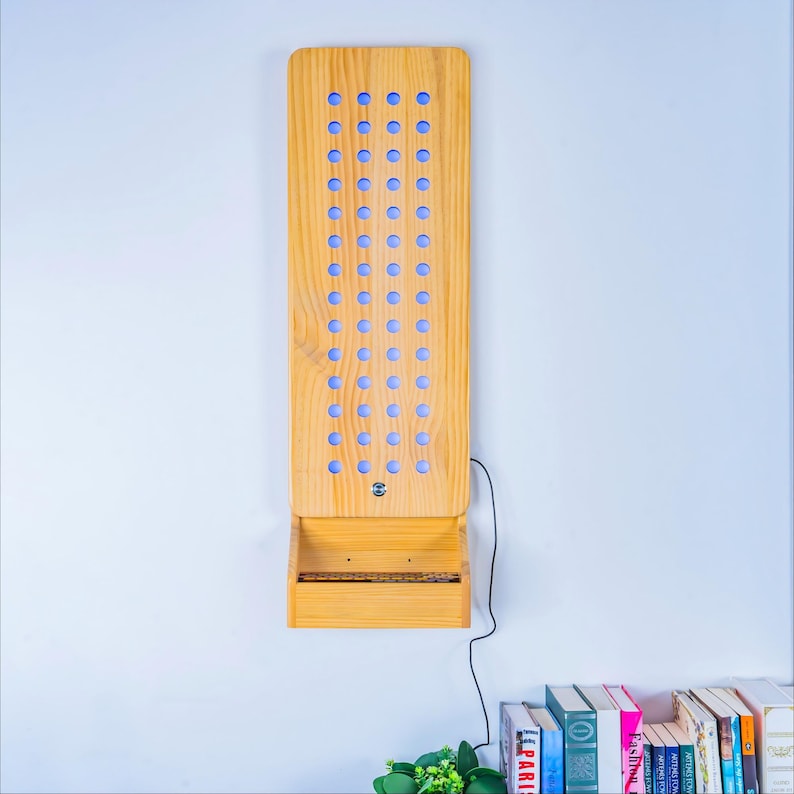 May include: A vertical light wood wall-mounted display board featuring four columns of circular cutouts with blue light shining through. The unit includes a small integrated shelf at the bottom and a thin black power cord extending from the side.