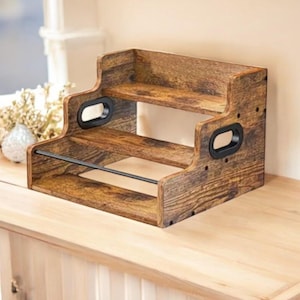 May include: A two-tiered wooden shelf with a distressed finish. The shelf has a dark brown stain, black handles, and a metal bar. It is designed for storage and display, suitable for kitchen or home decor.