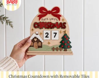 Könnte beinhalten: Ein hölzernes Weihnachts-Countdown-Schild mit einer roten Schleife oben, dem Text "DAYS UNTIL CHRISTMAS", einem braunen Haus mit Schnee, einem grünen Weihnachtsbaum und zwei weißen, herausnehmbaren Kacheln mit der Zahl 27 und goldenen Sternen.