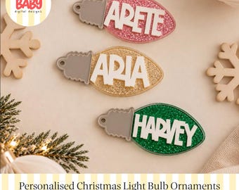 Könnte beinhalten: Drei weihnachtliche Glühbirnen-Ornamente mit glitzernden rosa, goldenen und grünen Oberflächen und weißer erhabener Schrift, die die Namen Arete, Aria und Harvey bilden. Jedes Ornament hat einen grauen Sockel mit einem Loch.