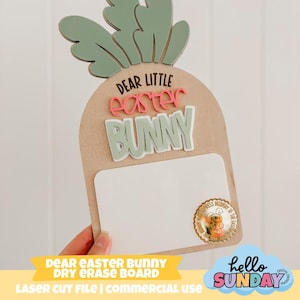 May include: A wooden carrot-shaped dry erase board with the text "DEAR LITTLE Easter BUNNY". The board has a white writing surface and a green carrot top. A small round sticker with a bunny is on the bottom right.