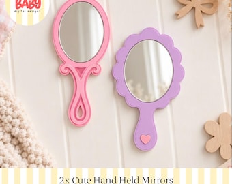 Könnte beinhalten: Zwei Handspiegel mit ovalen Spiegelflächen. Ein Spiegel hat einen rosa Rahmen mit einem dekorativen geschwungenen Griff. Der andere Spiegel hat einen lavendelfarbenen, gewellten Rahmen und einen Griff mit einem kleinen rosa Herz.