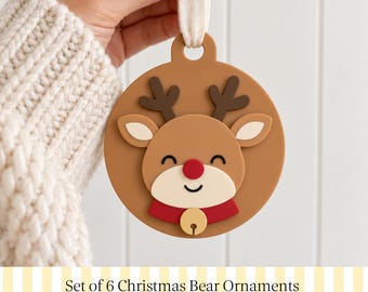 May include: A circular tan ornament featuring a raised reindeer design with dark brown antlers, a red nose, and a red collar with a gold bell. The ornament has a cream-colored fabric loop at the top for hanging. Text below reads Set of 6 Christmas Bear Ornaments.