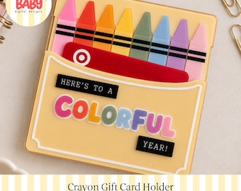 Könnte beinhalten: Ein hellgelber Geschenkkartenhalter in Form einer Buntstiftbox mit einer Reihe bunter Stifte oben. Auf der Vorderseite steht der Text "HERE'S TO A COLORFUL YEAR!" in schwarzen und bunten Buchstaben. Eine rote Geschenkkarte mit Zielscheiben-Logo steckt darin.
