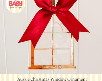 Könnte beinhalten: Ein fensterförmiger Anhänger aus roségoldenem Spiegelacryl mit einem viergeteilten Gitterdesign und dem eingravierten Text CHRISTMAS 2026 am unteren Rand. Ein leuchtend rotes Satinband ist oben zu einer großen Schleife zum Aufhängen gebunden.