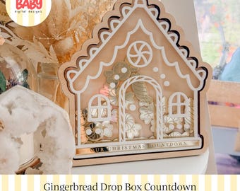 Könnte beinhalten: Eine hölzerne Drop-Box in Form eines Lebkuchenhauses mit einer transparenten Frontplatte. Der Rahmen hat weiße Verzierungen, ein Pfefferminz-Wirbelmuster und den Text OUR CHRISTMAS COUNTDOWN. Im Inneren befinden sich goldfarbene, bonbonförmige Plättchen.