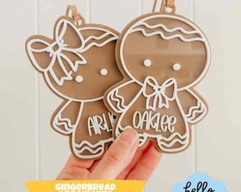 May include: Two gingerbread man ornaments with white outlines and bows. One ornament says "Arly" and the other says "Oaklee". The ornaments are held in front of a white background. The image also includes the text "GINGERBREAD ORNAMENTS" and "hello SUNDAY".