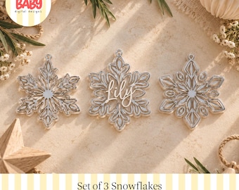 Könnte beinhalten: Drei silberfarbene Schneeflocken-Ornamente mit komplexen Ausschnittmustern. Die mittlere Schneeflocke zeigt den Namen Lily in weißer Schreibschrift. Jede Schneeflocke hat eine kleine kreisförmige Öse zum Aufhängen.