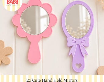 Könnte beinhalten: Zwei Handspiegel mit reflektierenden Oberflächen. Ein Spiegel hat einen rosa Rahmen in Blumenform mit einem abgerundeten Griff. Der andere Spiegel hat einen lavendelfarbenen Rahmen mit einer Schleife am Griff und einer herzförmigen Aussparung.