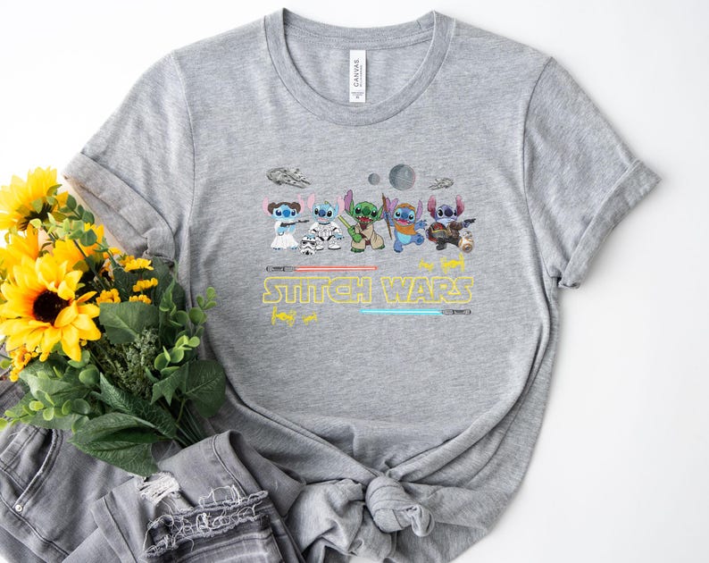 May include: A gray t-shirt featuring a graphic of several cartoon characters in a Star Wars theme. The text "Stitch Wars" is printed in yellow with blue and red lightsabers. The shirt is made of a soft material.