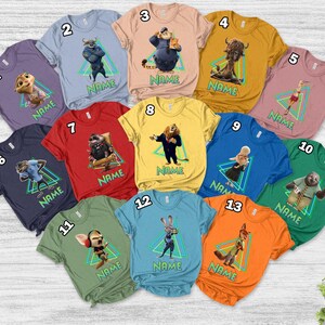 May include: A selection of short-sleeved t-shirts in various colours, each featuring a character from a movie. Each shirt has a character image inside a green and blue triangle, with the word "NAME" below the image.