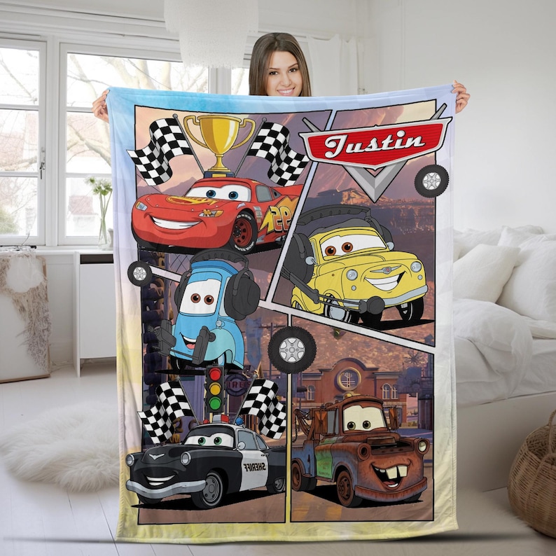 K&ouml;nnte beinhalten: Eine rechteckige Fleecedecke mit einem farbenfrohen Grafikdruck von Charakteren aus dem Film Cars. Das Design zeigt ein rotes Rennauto, ein gelbes Auto, ein blaues Auto, ein schwarz-wei&szlig;es Polizeiauto und einen braunen Abschleppwagen mit dem Namen Justin.