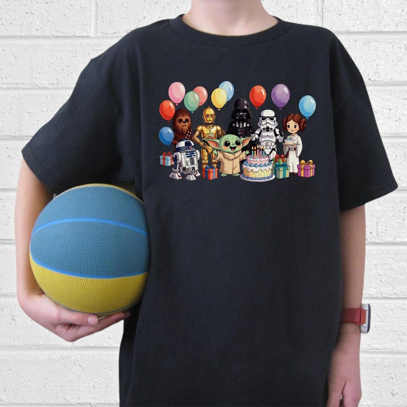 Puede incluir: Una camiseta azul marino con un gr&aacute;fico colorido de personajes de Star Wars celebrando un cumplea&ntilde;os. El dise&ntilde;o incluye a Yoda, Darth Vader y R2-D2, junto con globos y una tarta de cumplea&ntilde;os. Un ni&ntilde;o sostiene un bal&oacute;n de baloncesto azul y amarillo.