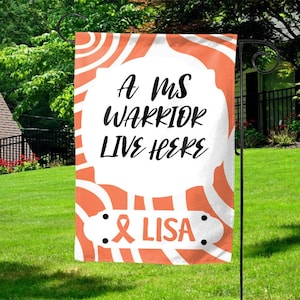 May include: A garden flag with the text "A MS WARRIOR LIVE HERE" in black script on a white background. The flag has an orange and white swirl design and includes the text "& LISA" with an orange ribbon symbol.