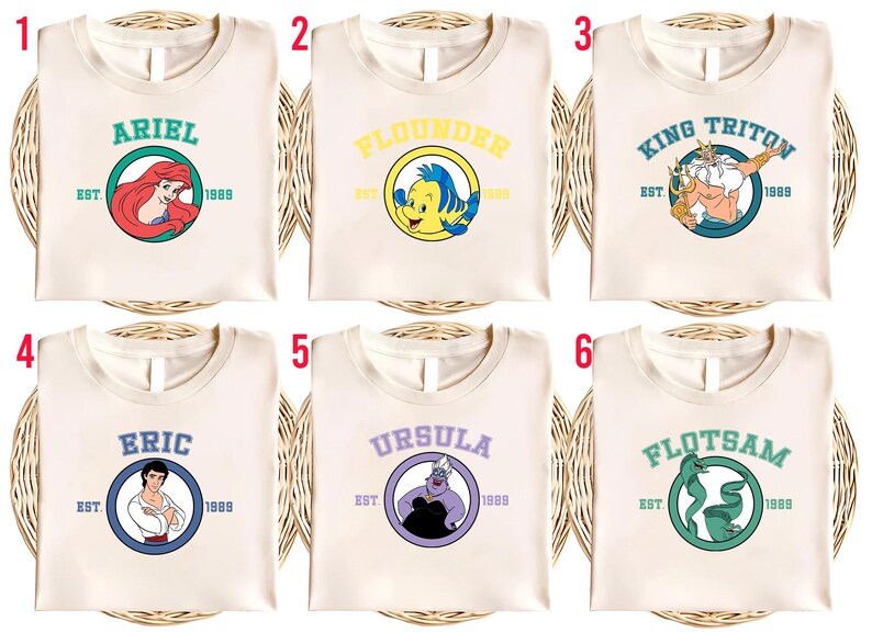 Puede incluir: Seis camisetas color crema con dise&ntilde;os de personajes de La Sirenita. Cada camiseta presenta el nombre de un personaje en un c&iacute;rculo con "EST. 1989". Los personajes incluyen Ariel, Flounder, Rey Trit&oacute;n, Eric, &Uacute;rsula y Flotsam.
