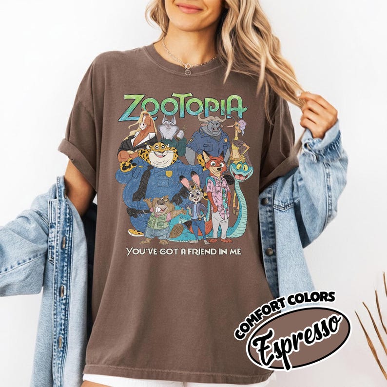 May include: Brown t-shirt featuring a colorful graphic of characters from the animated film "Zootopia." The design includes the film's title and the phrase "You've got a friend in me." The shirt is labeled "Comfort Colors Espresso."