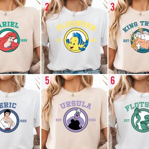 Puede incluir: Seis camisetas con personajes de una popular pel&iacute;cula animada. Cada camiseta muestra el nombre de un personaje en un c&iacute;rculo con el a&ntilde;o "1989" y "EST." Los personajes incluyen a Ariel, Flounder, Rey Trit&oacute;n, Eric, &Uacute;rsula y Flotsam.