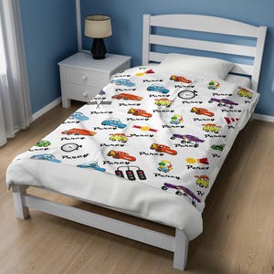 May include: A white blanket featuring a repeating pattern of colorful cartoon race cars, stoplights, checkered flags, and stopwatches, interspersed with the name Percy printed in a black script font across the fabric surface.